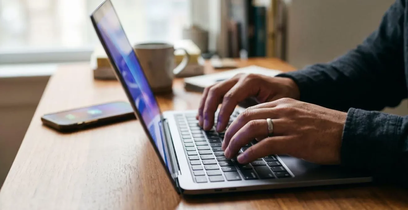 Mains tapant sur un clavier avec smartphone affichant notification urgente en arrière-plan